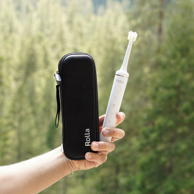 Étui de voyage Rolla noir avec logo blanc, tenu en main à côté de la brosse à dents électrique Rolla